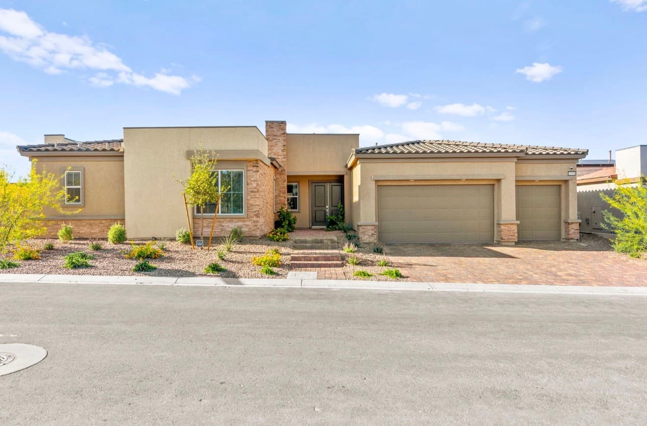 Modern tan single-story house with stone accents, a three-car garage, and desert landscaping.
